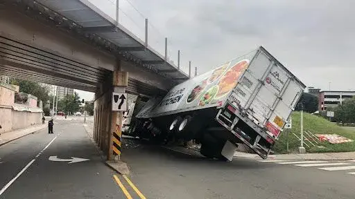 A truck accident leaves the truck stuck on a bridge at a semi-overturned angle, causing property damage.